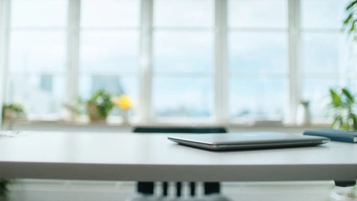 A modern minimal software studio workspace with a clean desk and bright city windows